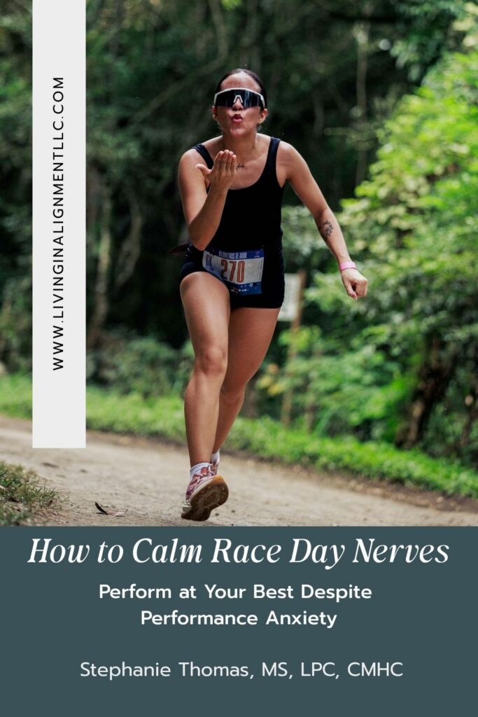 A female runner in a black outfit blowing a kiss to the camera during a race, featured on a Pinterest-style blog graphic for Living in Alignment LLC titled "How to Calm Race Day Nerves and Perform at Your Best Despite Performance Anxiety" by Stephanie Thomas.