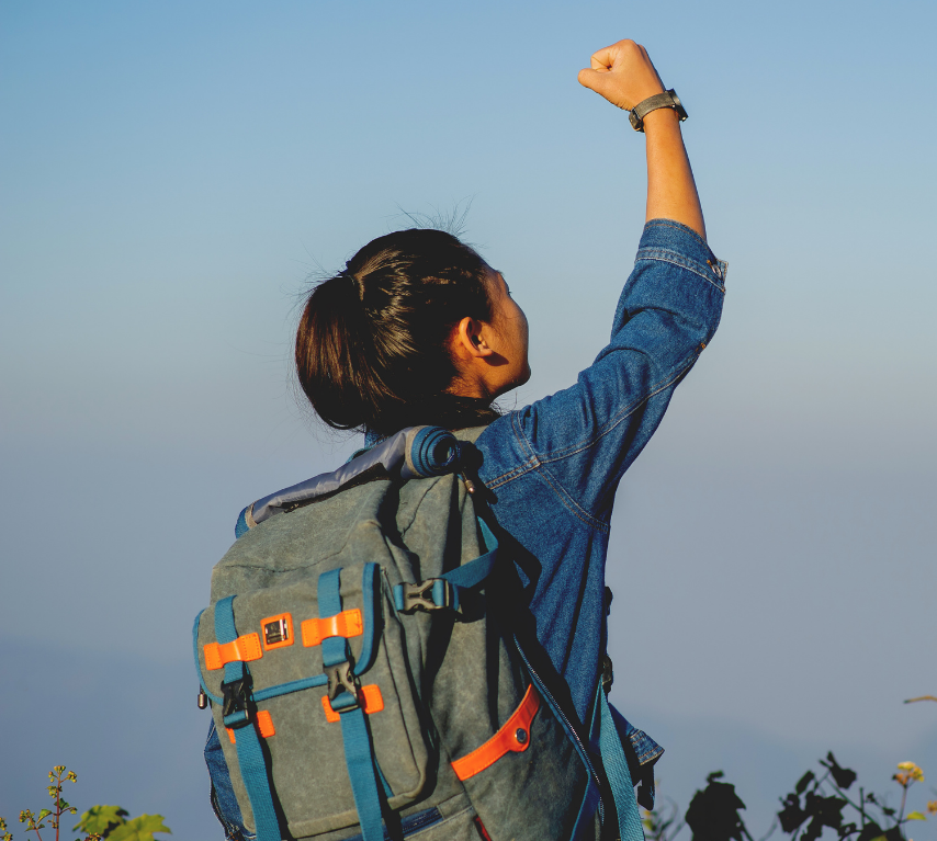 Woman raising her fist in triumph on a mountain trail at sunrise, symbolizing balanced success for high achievers